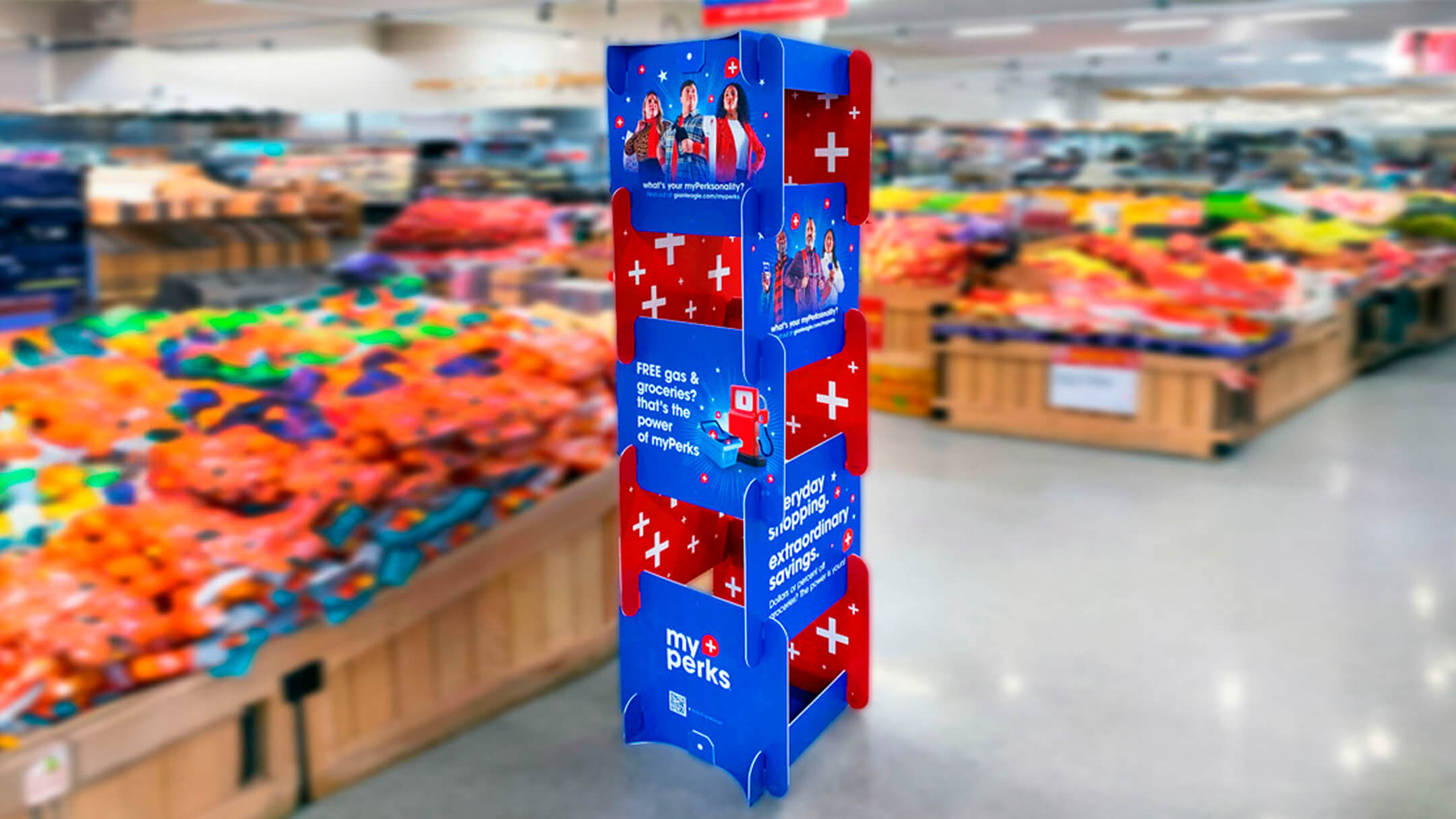 Tall freestanding myPerks grocery display with promotional messages about free gas, groceries, and rewards, placed in the produce section.