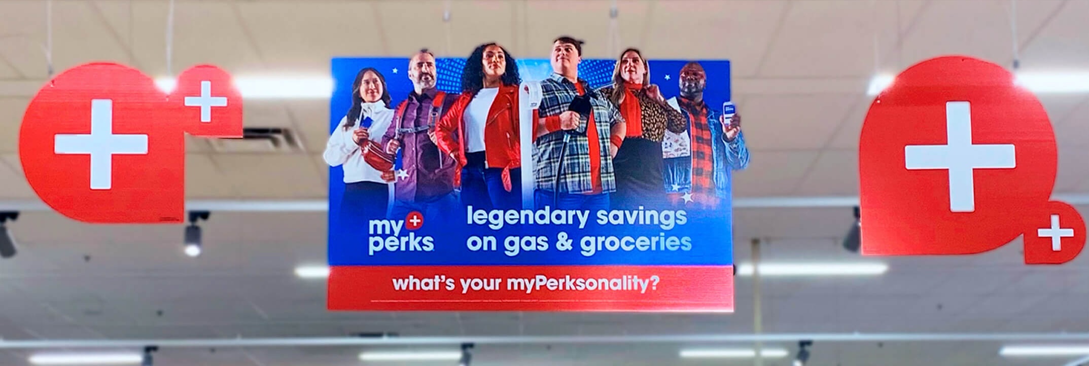 Large hanging sign in grocery store advertising myPerks savings with six diverse people and red plus icons on either side.