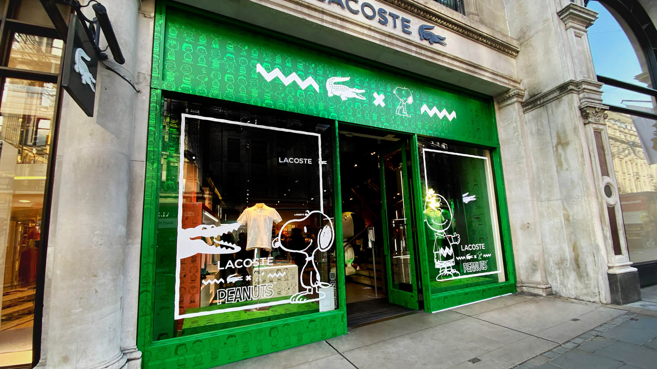 Lacoste retail storefront decorated for Peanuts collaboration featuring Snoopy and Charlie Brown illustrations on glass.