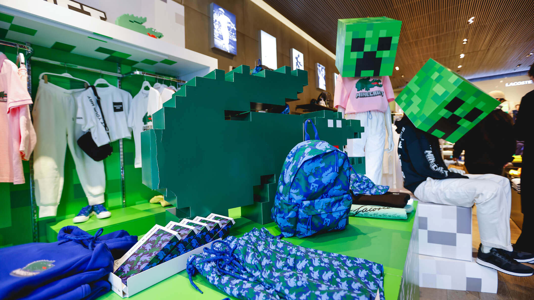 Lacoste x Minecraft retail display with pixelated crocodile decor, themed apparel, and mannequins wearing Minecraft Creeper heads.