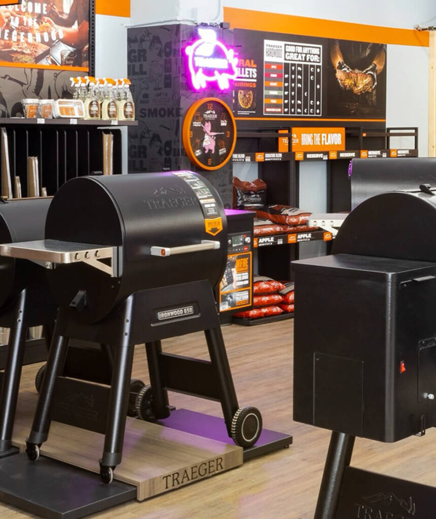 Traeger Ironwood 650 grills on display in a retail showroom with wood pellet products and promotional signage.