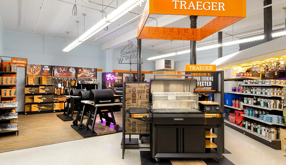 Traeger Timberline XL grill showcased in a hardware store retail setting with accessories and other grills in the background.