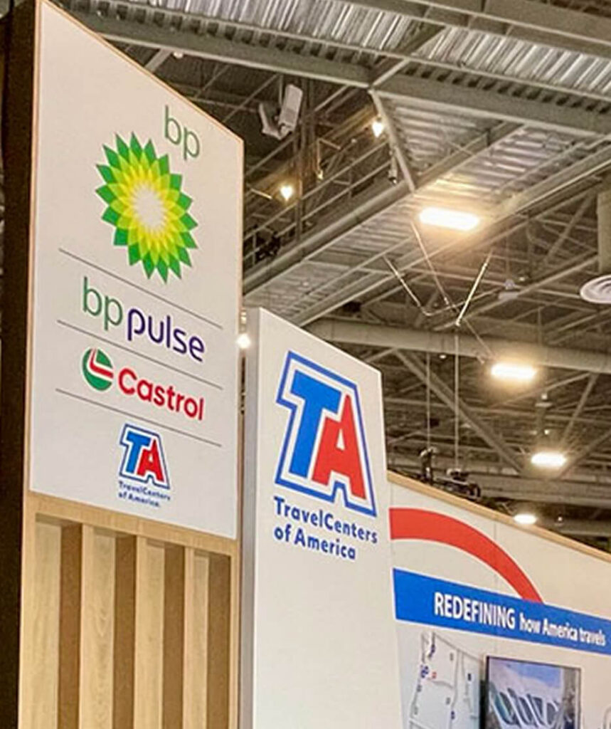 Trade show signage with logos of bp, bp pulse, Castrol, and TravelCenters of America displayed on wooden and white vertical panels.