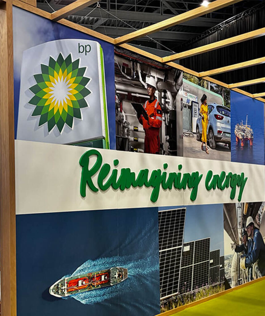 Exhibition wall with BP’s logo and the slogan “Reimagining energy,” surrounded by images of energy infrastructure, workers, solar panels, and transportation.