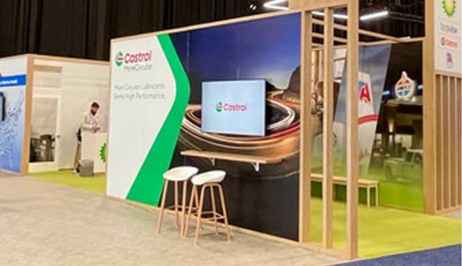 Castrol exhibition booth with branded wall display, screen, and seating area.