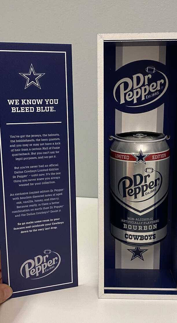 Interior of a limited-edition Dr Pepper box featuring a can of non-alcoholic bourbon-flavored soda co-branded with the Dallas Cowboys, alongside a message printed on the box flap.