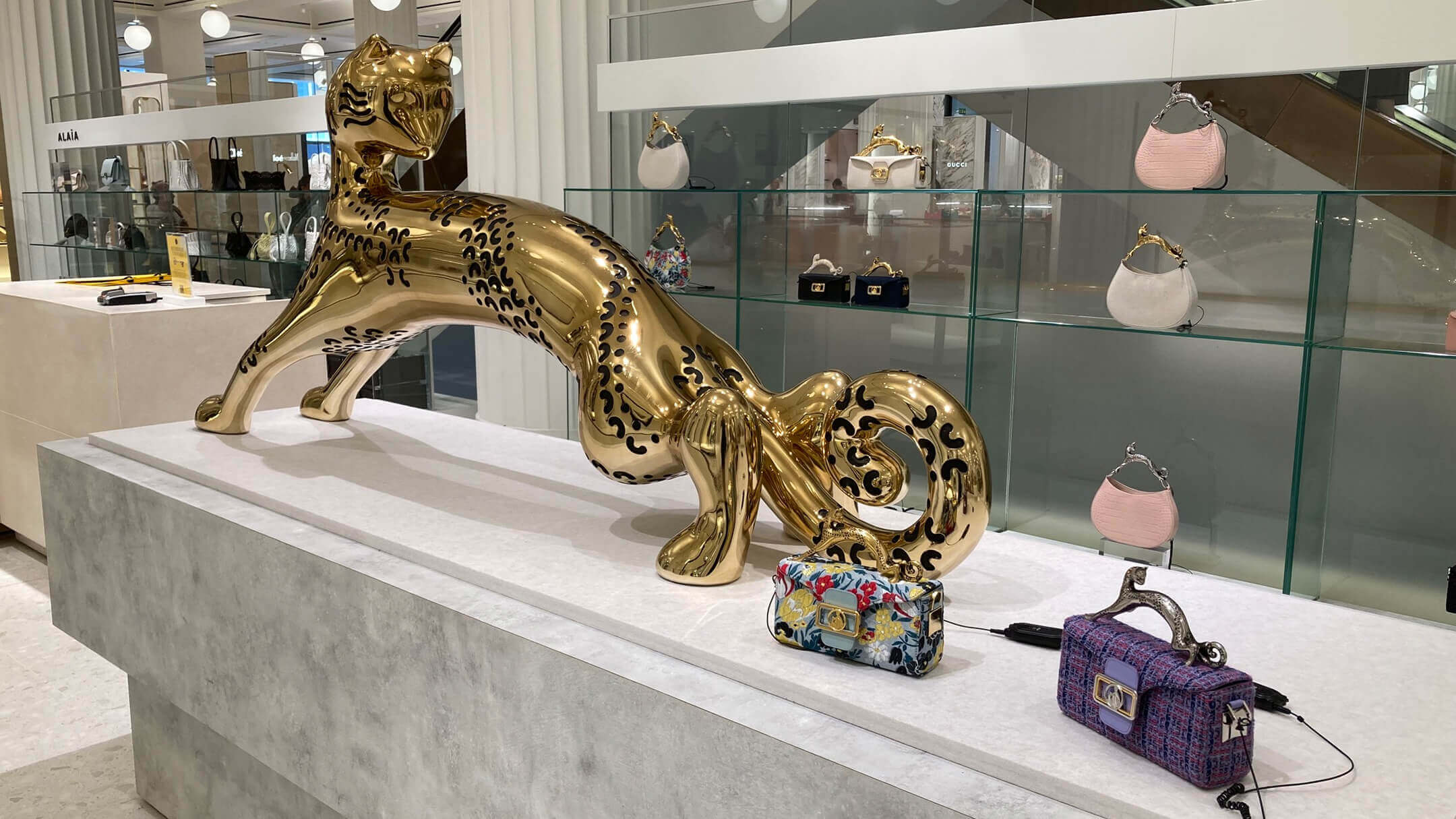 Close-up of a Lanvin retail display featuring a polished gold feline sculpture surrounded by luxury handbags on a stone pedestal.