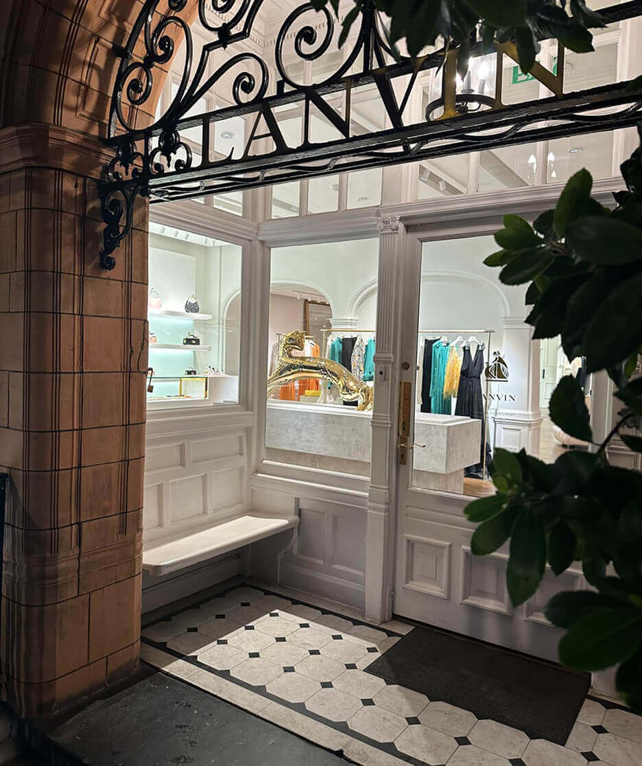 Elegant exterior view of a Lanvin boutique with black wrought iron signage, classic tiled entryway, and a glimpse of the interior display featuring a gold sculpture and luxury fashion.