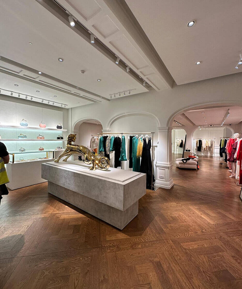 Interior of a Lanvin boutique featuring elegant archways, wood flooring, luxury dresses on display, designer handbags on glass shelves, and a central gold panther sculpture.